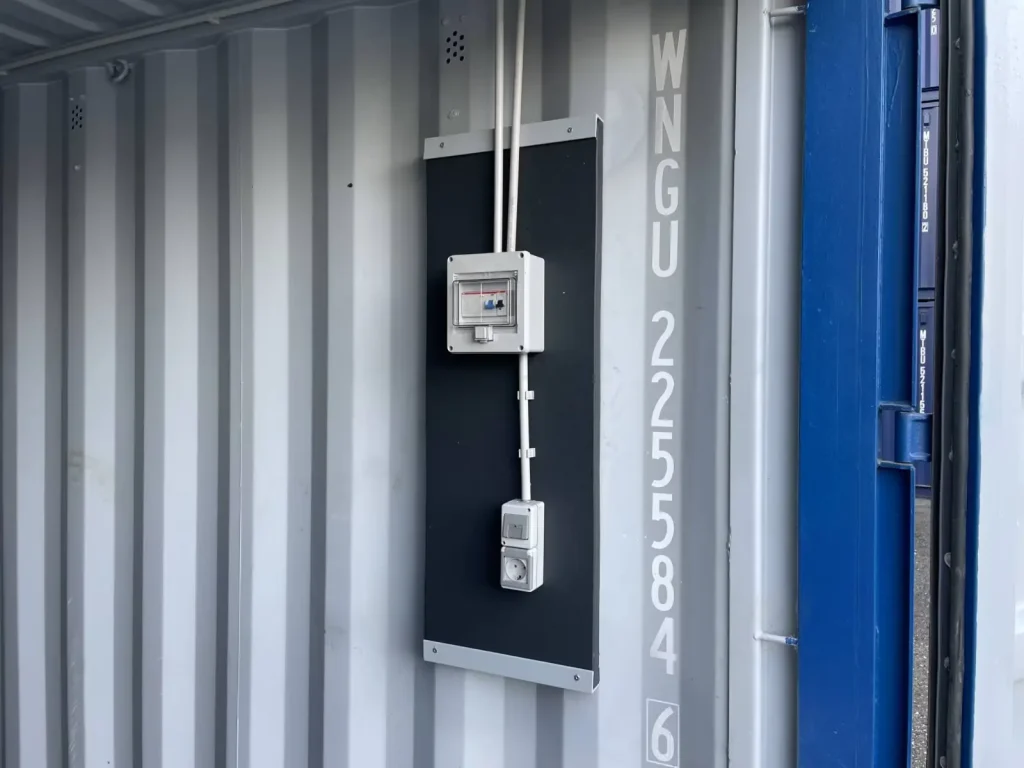 Elektro-Verteiler und Steckdose auf Montageplatte im Container – vorbereitet für Stromanschluss und Nutzung.